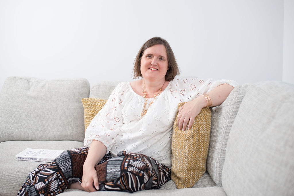 Deb sits on a sofa, smiling, looking to camera.